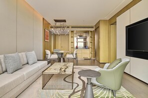 Una sala moderna con sofá, mesa de centro y sillas, un área de cocina con mesa de comedor y un televisor de pantalla plana montado en la pared.