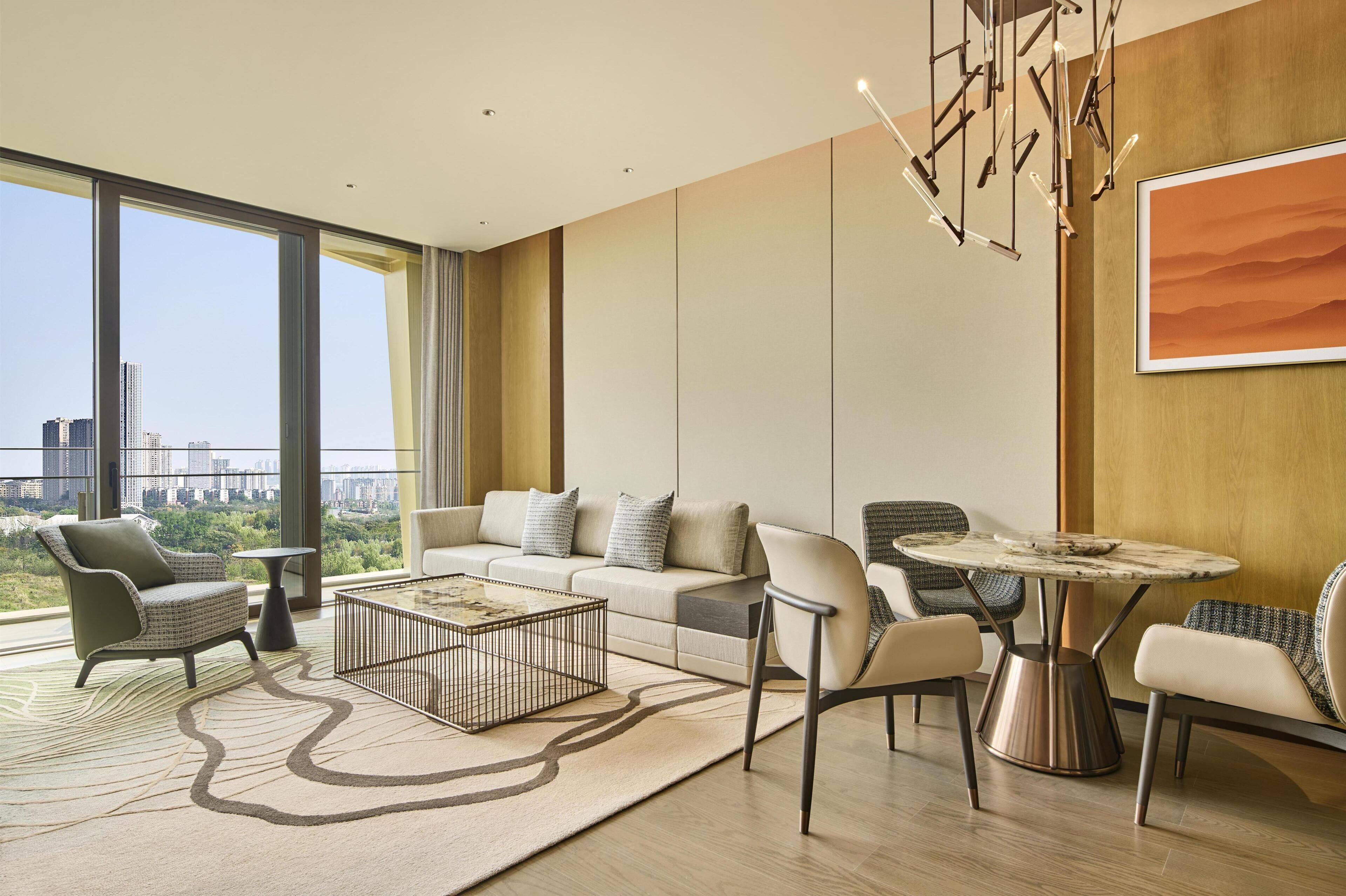 Un salon moderne avec un canapé, des fauteuils, une table basse et une vue sur le paysage urbain grâce à de grandes fenêtres.
