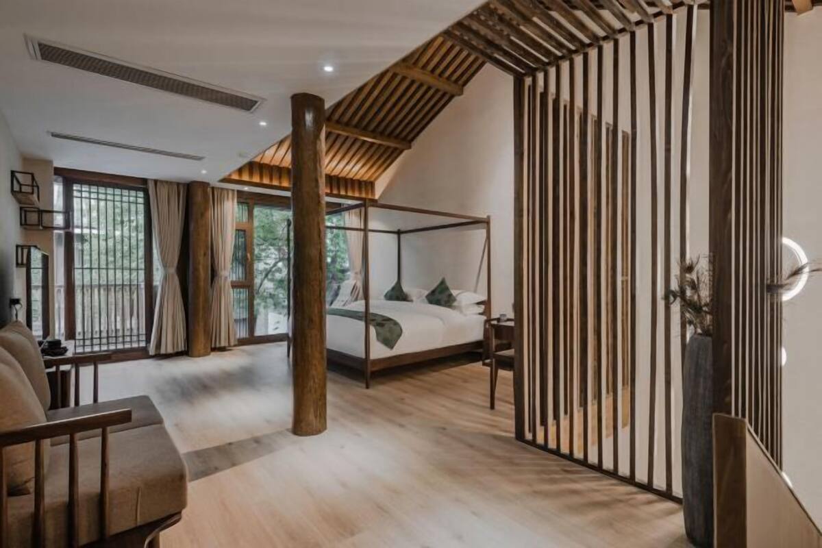 Un dormitorio moderno con cama de dos columnas, suelo de madera y ventanas amplias.