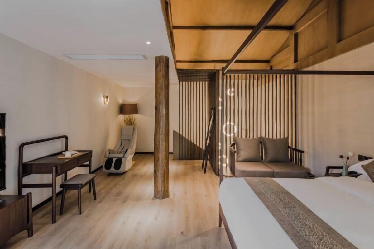 A modern hotel room with a wooden ceiling, a sofa bed, a desk with a chair, a TV, and a large window.