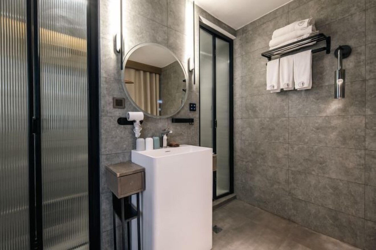 A modern bathroom with a white sink, a round mirror, a towel rack, and a glass shower enclosure.