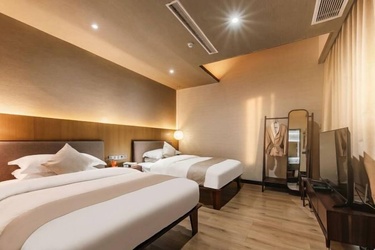 Habitación de hotel con dos camas, un espejo, un televisor y piso de madera.