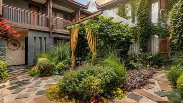 A courtyard with a stone pathway, lush greenery, and a wooden balcony.
