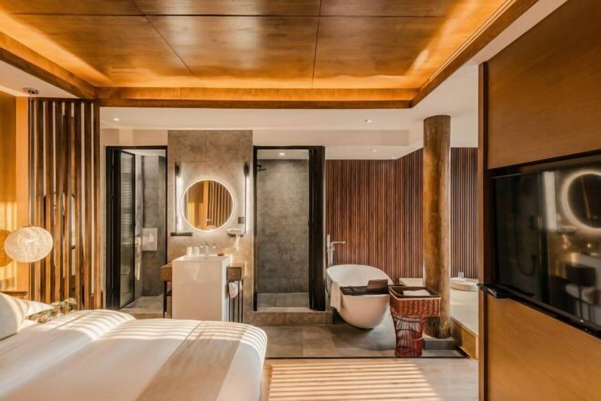 Una habitación de hotel moderna con techo de madera, una cama grande, un baño con bañera y un televisor.