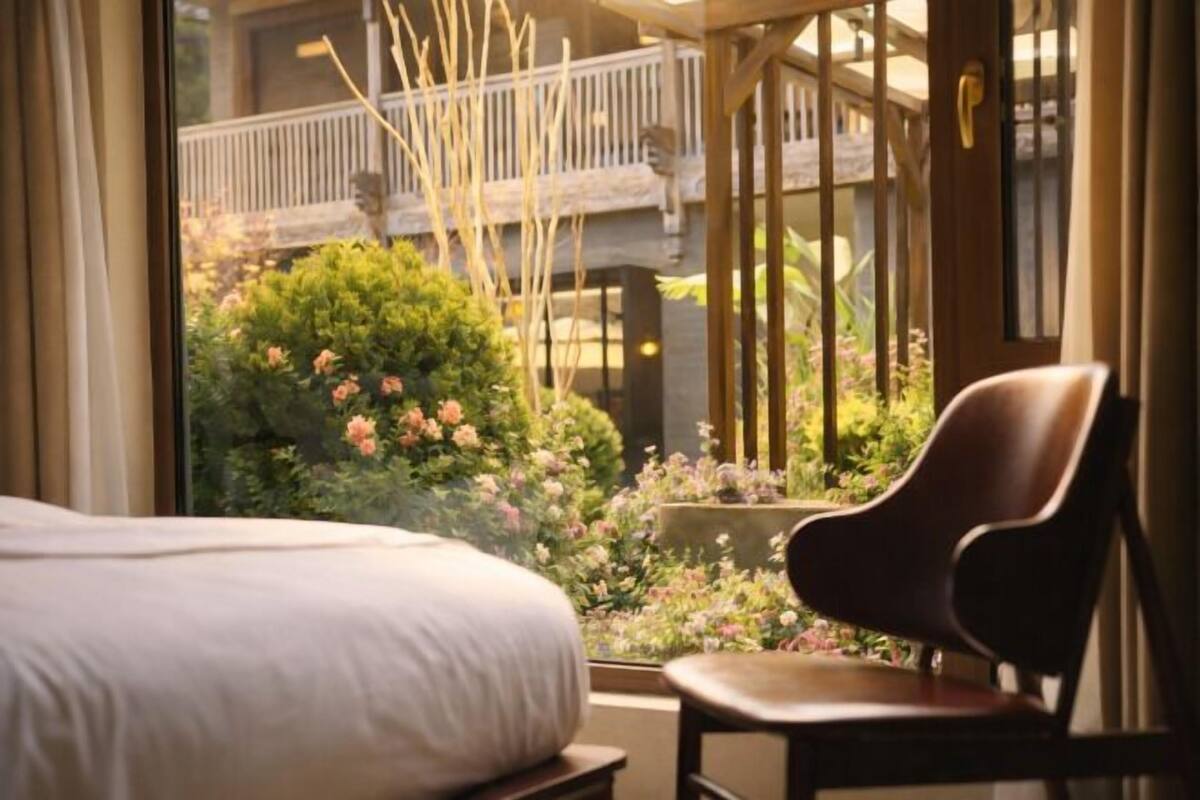 Habitación de hotel con cama, una silla y vistas a un balcón con plantas y una estructura de madera.