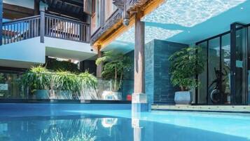 A modern pool area with a clear pool, wooden deck, and potted plants.