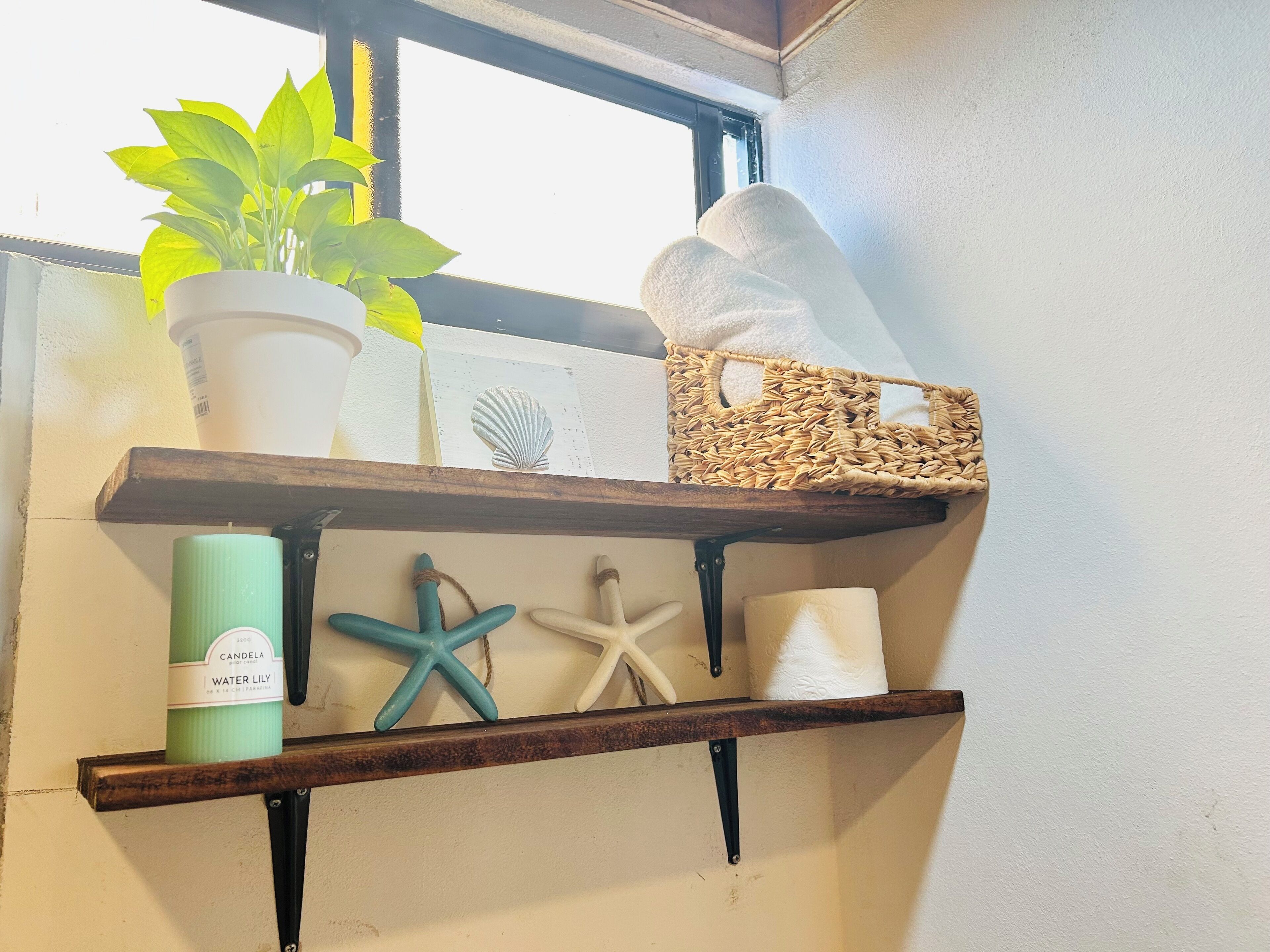 A shelf with a potted plant, a candle, a starfish, and a woven basket.