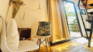 Un intérieur moderne avec un plafond en bois, un téléviseur à écran plat fixé au mur, une chaise blanche, un coussin décoratif et une vue sur l’extérieur grâce à une grande fenêtre.