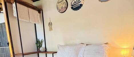 Quarto com teto de madeira, cama com colcha branca e duas decorações nas paredes.