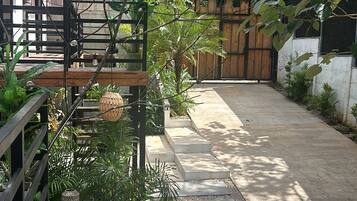 Un sendero en un jardín con escalones que conducen a un portón de madera, rodeado de abundante follaje y plantas en macetas.