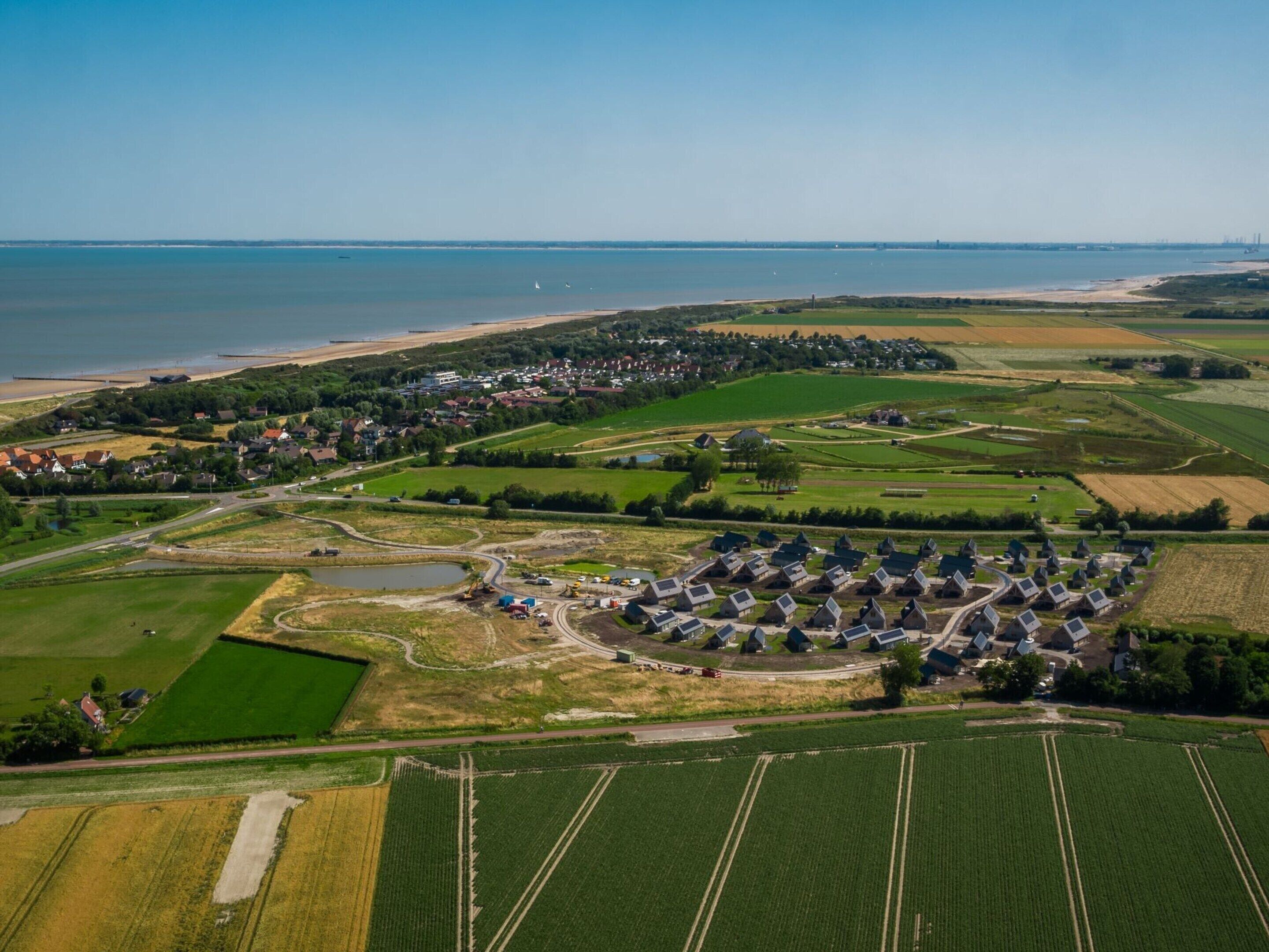 An aerial view of a rural area with fields, a small village, and a beach.