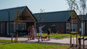 A family walking in front of a modern building with a metal roof and large windows. - Dune Lodge on a Holiday Park, Beach at 1.3 km (Cadzand-Bad)