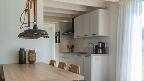 A modern kitchen with white cabinets, a wooden dining table, and wicker chairs. - Dune Lodge on a Holiday Park, Beach at 1.3 km (Cadzand-Bad)