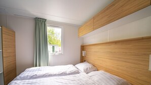 A bedroom with two beds, a window with curtains, and wooden headboards. - Colorful Chalet Near Amsterdam (Amstelveen)
