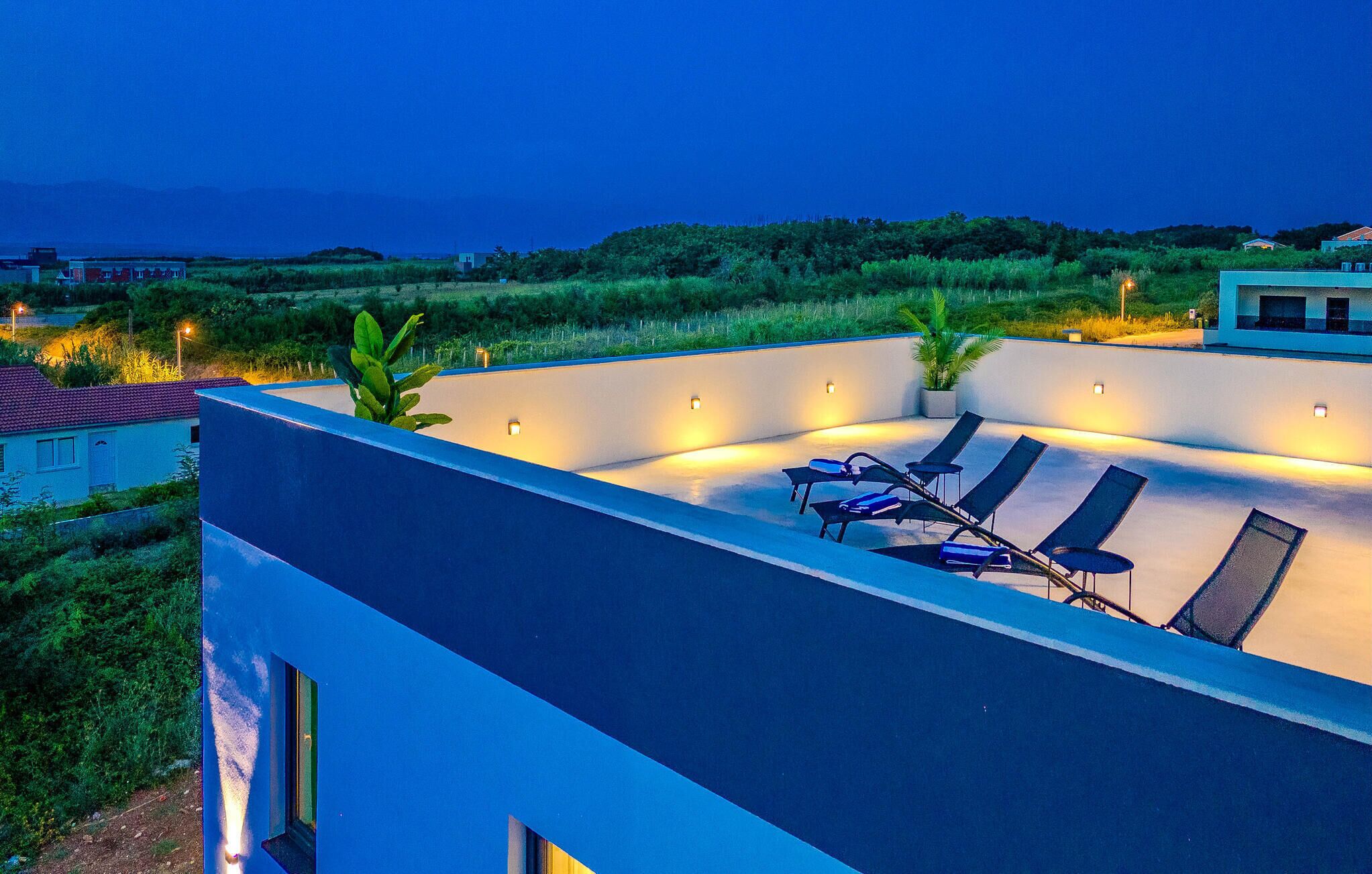 Eine Dachterrasse mit Liegestühlen und stimmungsvoller Beleuchtung, mit Blick auf eine üppige Landschaft.
