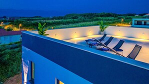 A rooftop terrace with lounge chairs and ambient lighting, overlooking a lush landscape. - Gorgeous home in Privlaka (Privlaka)