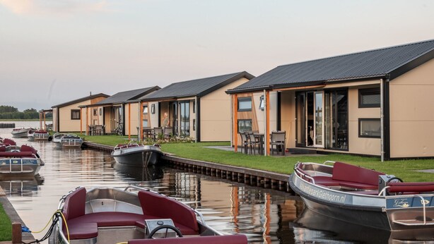 A row of modern, single-story houses with large windows and a canal in front. - Fenced Garden Family Chalet (Giethoorn)