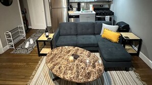 Uma sala de estar moderna com um sofá seccional, uma mesa de centro redonda e uma cozinha ao fundo.