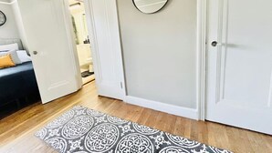 Um corredor com tapete estampado, espelho redondo e cama com cabeceira escura.
