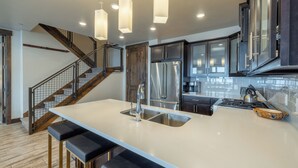 Una cocina moderna con una isla central, electrodomésticos de acero inoxidable y una escalera con detalles de madera.