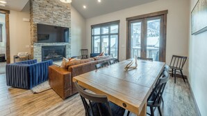 Un comedor moderno con una mesa y sillas de madera, una chimenea de piedra y un amplio ventanal con vistas al exterior.
