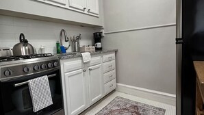 Una cocina con armarios blancos, una estufa de acero inoxidable, un refrigerador negro y una alfombra estampada.