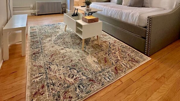 Un dormitorio con cama, ventilador de techo, mesita de noche, alfombra y ventana.