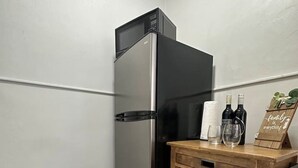 Una habitación en esquina con un refrigerador de acero inoxidable, un carrito de madera con botellas y vasos, y una alfombra estampada.