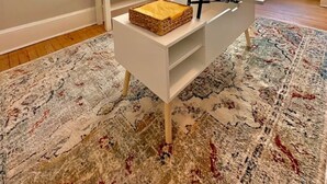 Una sala moderna con un televisor de pantalla plana montado en la pared, un sofá blanco, una mesa de comedor y una alfombra estampada.