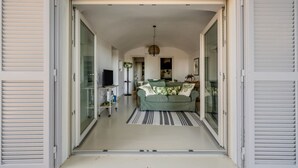 An open sliding door leading to a living room with a sofa, a television, and a striped rug. - White Conus by Rentbeat (Ostuni)