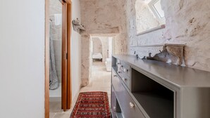 A narrow hallway with a stone wall, a wooden door, a patterned rug, and a modern dresser. - White Conus by Rentbeat (Ostuni)