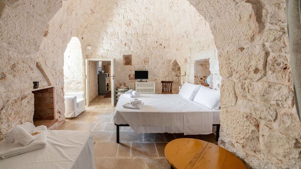 A stone-walled bedroom with a bed, a wooden chair, and a television. - White Conus by Rentbeat (Ostuni)