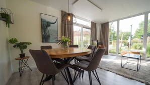 Een moderne eetruimte met een ronde houten tafel, donkere gestoffeerde stoelen en een hanglamp.