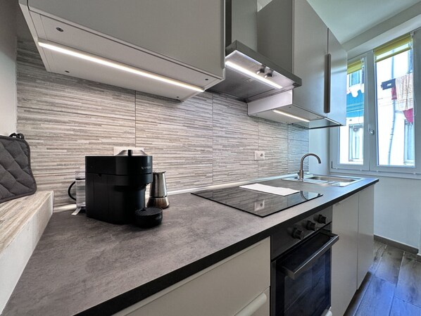 A modern kitchen with a built-in stove, a coffee maker, and a window with a view of the outside.