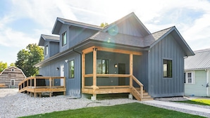 Ett modernt hus i två våningar med en inglasad veranda och en liten terrass, omgivet av en grusuppfart och en gräsplätt.