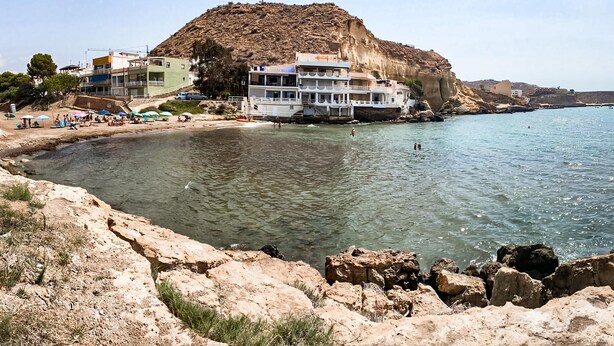 Un hôtel en bord de mer, adossé à une falaise rocheuse, avec une plage et une eau cristalline.