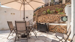 Une terrasse extérieure avec une table et des chaises, un grand parasol et un mur de pierre orné de plantes.