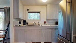 A compact kitchen with white cabinets, a window above the sink, and a stainless steel refrigerator. - Classic Maine Cabin, Private Waterfront Easy Access to Nearby Amenities (Windham)