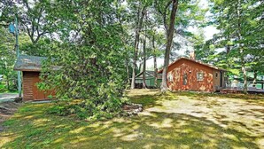 A rustic cabin with a small shed, surrounded by dense trees and a grassy yard. - Classic Maine Cabin, Private Waterfront Easy Access to Nearby Amenities (Windham)