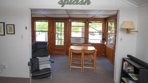 A room with a wooden table and chairs, a black chair with a patterned cushion, a bookshelf, and a sign that reads "Splash" on the wall. - Classic Maine Cabin, Private Waterfront Easy Access to Nearby Amenities (Windham)