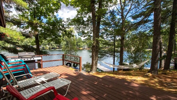 A wooden deck with outdoor seating, a hammock, and a view of a lake. - Classic Maine Cabin, Private Waterfront Easy Access to Nearby Amenities (Windham)