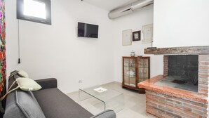 A living room with a grey sofa, a glass coffee table, a brick fireplace, a TV mounted on the wall, and a cabinet with glass doors. - Beautiful apartment in Filignano with WiFi (Filignano)