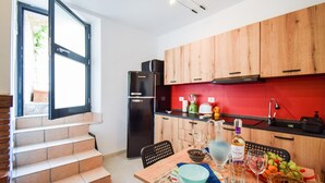 A modern kitchen with wooden cabinets, a black refrigerator, and a red backsplash. There is a dining table with plates, a bowl, and a bottle of GLICINE. - Beautiful apartment in Filignano with WiFi (Filignano)