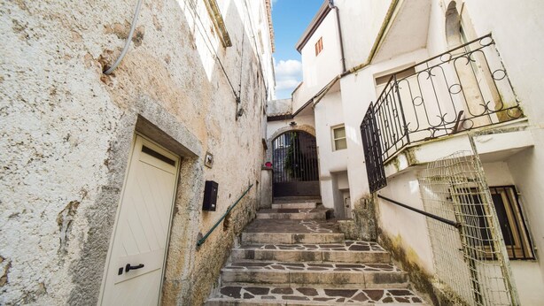 A narrow stone staircase leading up to a building entrance, flanked by white walls with visible wear and a metal gate. - Beautiful apartment in Filignano with WiFi (Filignano)