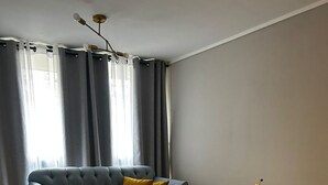 Ein modernes Wohnzimmer mit grauem Sofa, gelben Sesseln, einem Glastisch und einem kleinen Beistelltisch mit Pflanze.