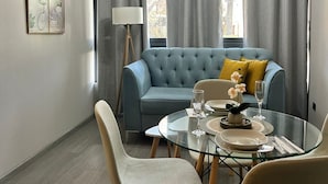 Ein modernes Wohnzimmer mit einem blauen Sofa, einem Glastisch mit Stühlen und einer Stehlampe.