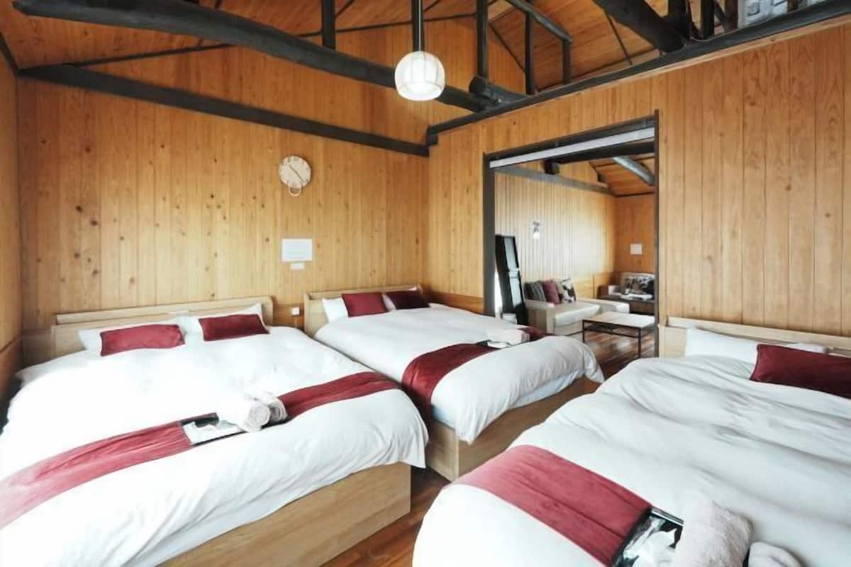 Quarto com três camas de madeira, teto de madeira e uma pequena mesa com uma cadeira.