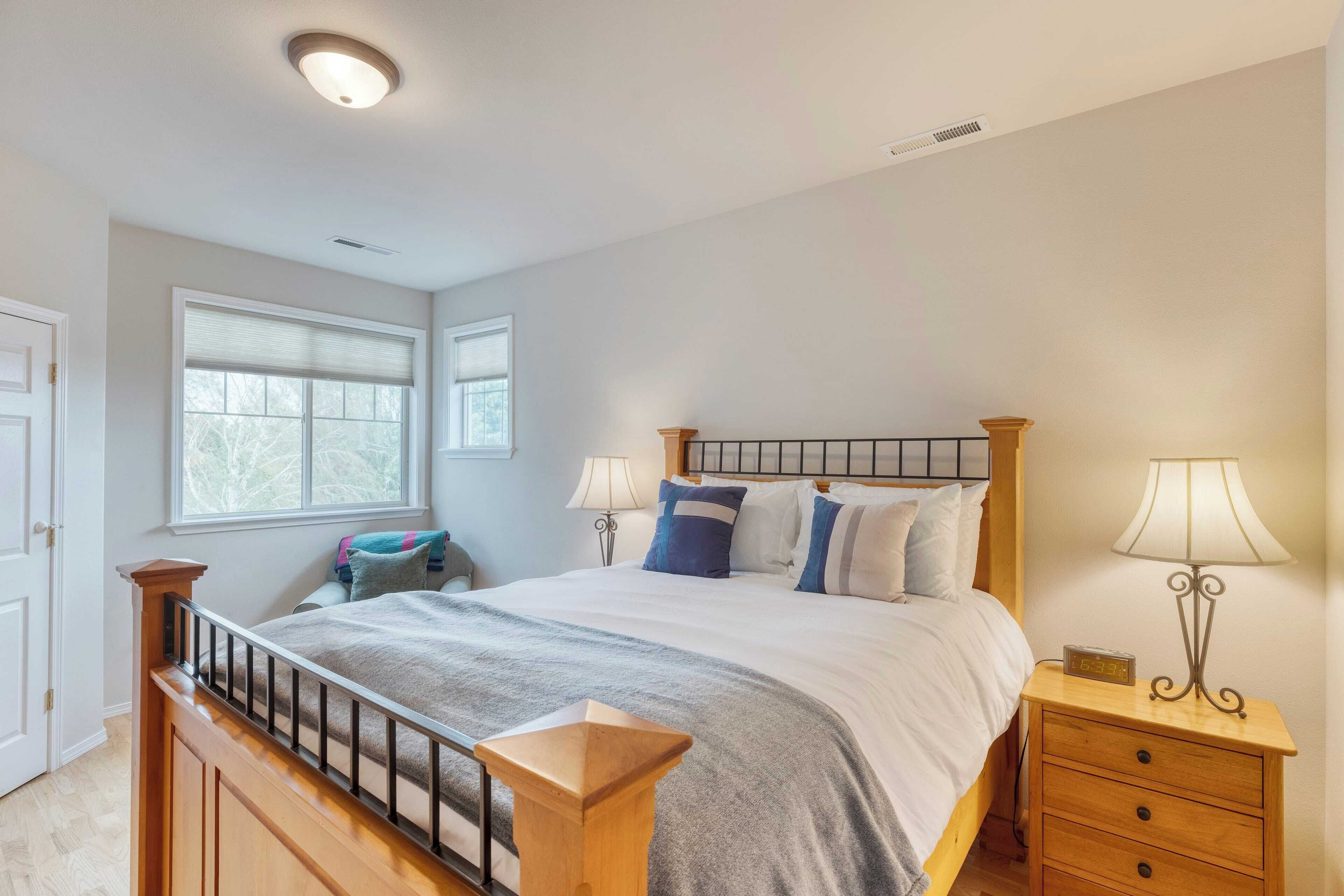 Une chambre à coucher avec un lit en bois, deux tables de chevet, une commode, une fenêtre et une porte.