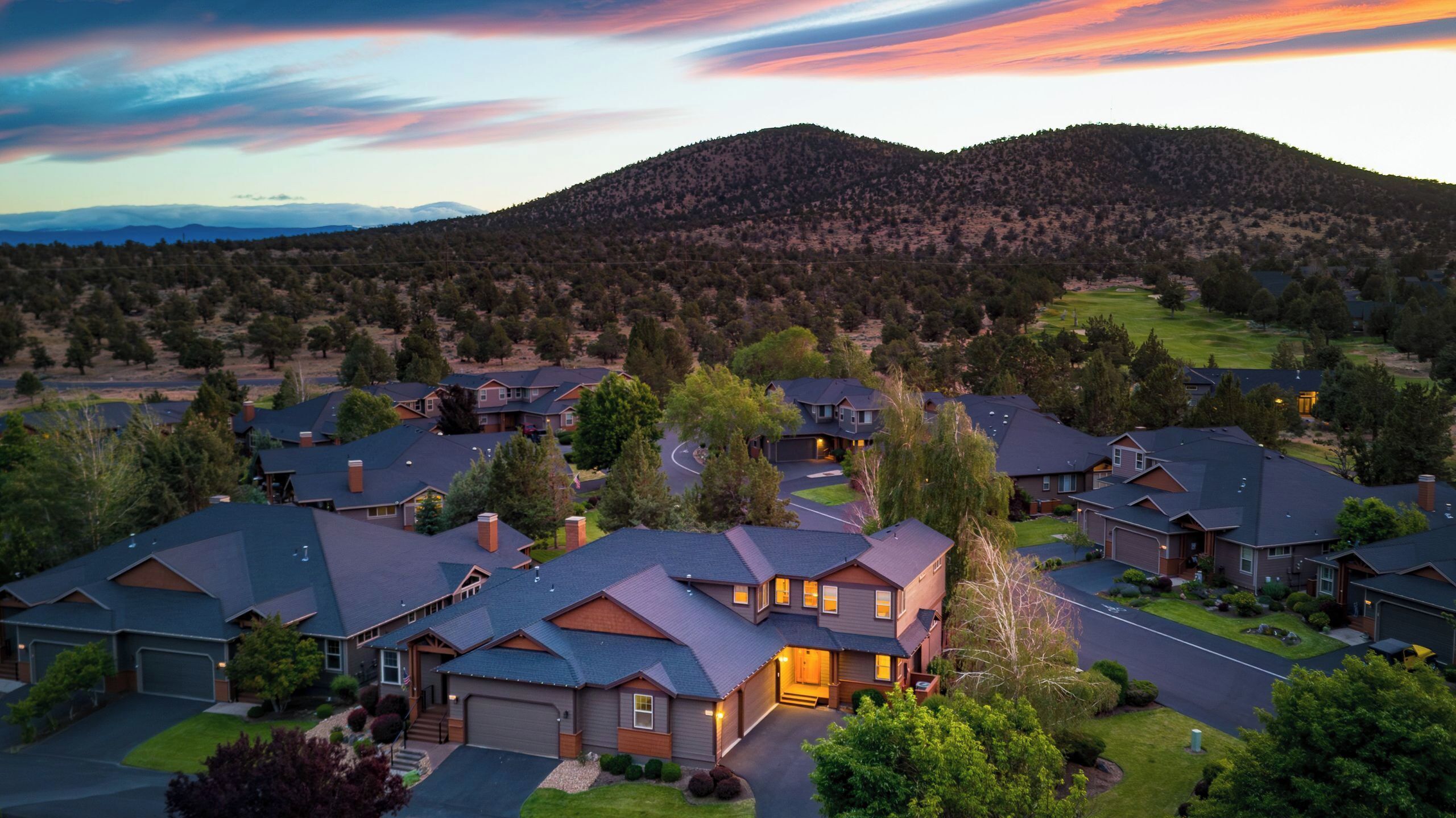 A residential area with houses, a driveway, and a hilly landscape in the background.