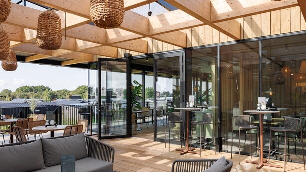 A spacious outdoor seating area with wooden flooring, wicker chairs, and a sofa. - Luxurious Lodge in a Holiday Park (Zwartewaal)